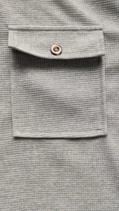 Detail of gray waffle texture fabric with a brown button on the square chest pocket