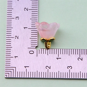 Detail shot of a small pink flower resin charm with gold metal base and measurement scale