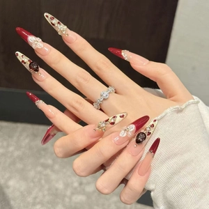Dettaglio di unghie finte fatte a mano di lusso con gemme rosse e fiori bianchi.