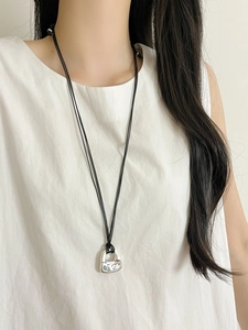 Detail of silver handbag pendant necklace on model wearing a white sleeveless top