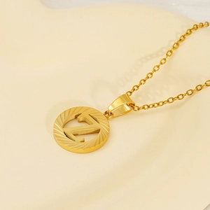 Golden 18K titanium steel letter necklace with sunray texture pendant on beige background