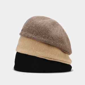 Three wool beret hats in brown, beige, and black stacked on a clean gray background