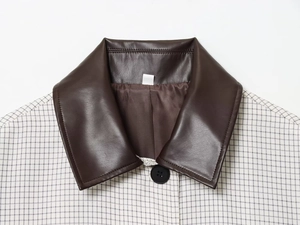 Détail du col en similicuir marron et motif à carreaux noirs sur veste courte
