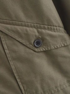 Detail of military green jacket showing cotton canvas texture and resin button pocket