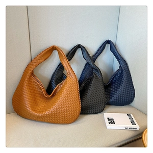 Three woven leather shoulder bags in caramel, black, and navy blue on a gray sofa