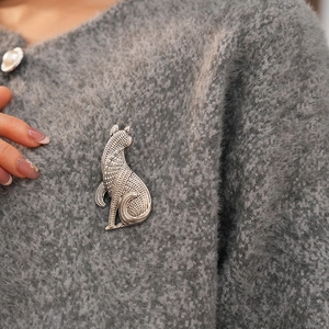 Detail einer Vintage Silber Metall Katzenbrosche mit Textur auf grauem Strickpullover