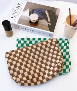 Flat lay of knit checkerboard makeup bags in brown and green on a white desk