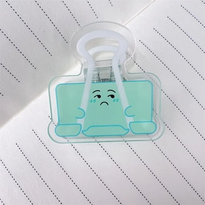 Nahaufnahme einer hellgrünen Acryl-Büroklammer mit traurigem Emoji auf liniertem Papier