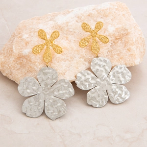 Macro detail of two-tone hammered metal flower earrings on a natural stone surface