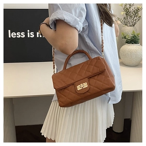 Lifestyle shot of a brown quilted crossbody bag with gold lock on a minimalist desk