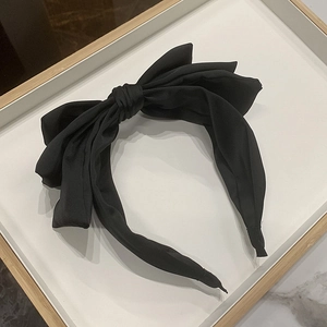 Top view of a black satin triple-layered bow headband on a minimal white wooden tray