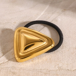 Golden geometric triangle hair tie with black rubber band on a textured stone surface