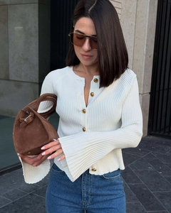 Close-up of white ribbed knit cardigan with gold embossed buttons and bell sleeves