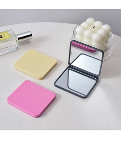 Detailed view of mini folding makeup mirrors in black, pink and yellow on a desk