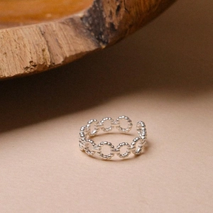 Detail view of silver open ring with textured circular links on a minimalist wooden background