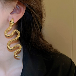 Close-up of golden snake-shaped long earrings with green gem eyes worn by a model