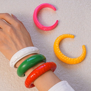 Dettaglio di bracciali aperti in acrilico colorato con trama increspata e design a C