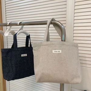 Close-up of beige and navy canvas tote bags with Simple Wish tags on white hangers