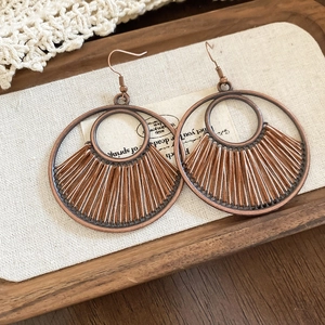 Detailed shot of vintage bronze hoop earrings with bohemian woven fan pattern on beige fabric