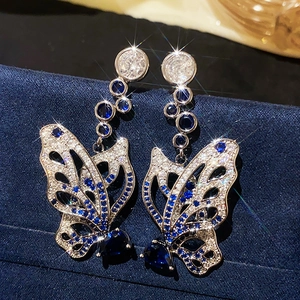 Macro shot of silver bow earrings with blue gems on a dark blue velvet background