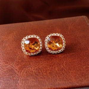 Détail de clous d'oreilles carrés ambrés avec placage or 18k et micro-cristaux sur cuir