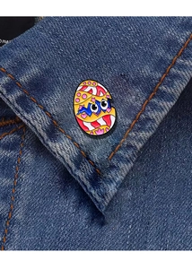 Detailed view of a cute colorful enamel dinosaur egg badge pinned on a denim jacket collar