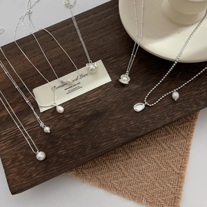 Elegant 925 sterling silver pearl necklace set with bow and shell pendants on wood base