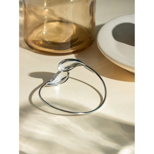 Detail of silver drop-shaped open bangle with polished fluid lines in natural sunlight