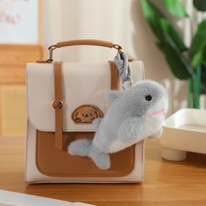 Close-up of cute plush shark keychain accessory hanging on a beige crossbody bag