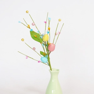 Easter floral branch with colorful eggs, faux berries and green leaves in a small vase