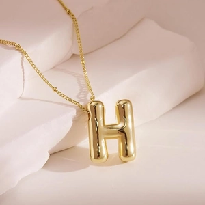 Close-up of golden letter H puffy pendant with polished surface on a fine bead chain