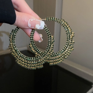 Dettaglio di grandi orecchini a cerchio dorati con cristalli pavé verde scuro e strass