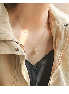Close-up of golden oval textured star pendant necklace worn by a woman with an elegant style