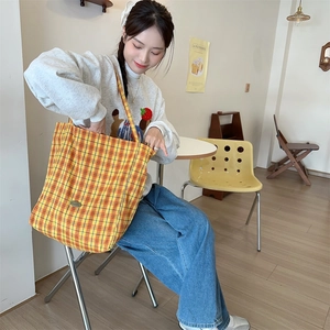 Close-up of yellow checkered canvas tote bag worn by a model in a cozy cafe setting
