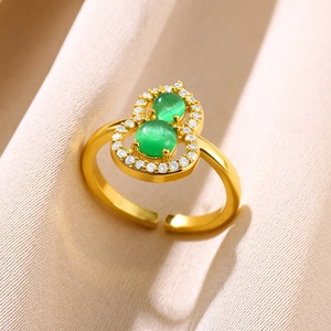 Close-up of golden gourd ring with green gemstones and zircon stones on soft fabric