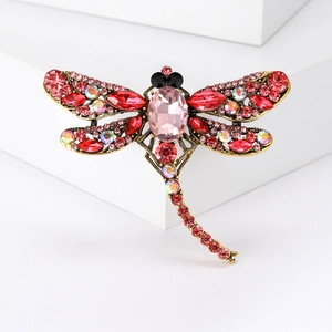 Detail of vintage bronze dragonfly brooch with red and pink crystals on white base