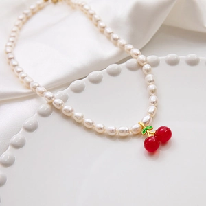 Macro shot of a red cherry pendant on a freshwater pearl necklace on a white ceramic plate