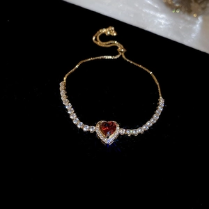 Macro shot of gold heart bracelet with red zircon and white stones on black background