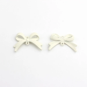 Detailed macro view of matte cream alloy bow charms with dual loops for DIY jewelry making