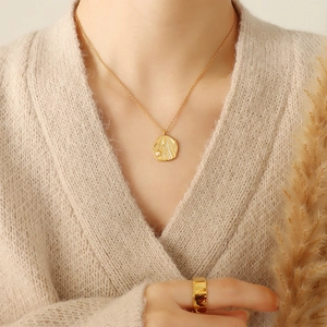 Golden pearl necklace with irregular textured pendant worn on a model with knitwear