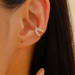Macro view of gold-tone X-shaped ear cuff with pave crystals worn on ear cartilage
