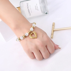 Minimalist cat eye bead bracelet with golden heart charm on a textured white fabric