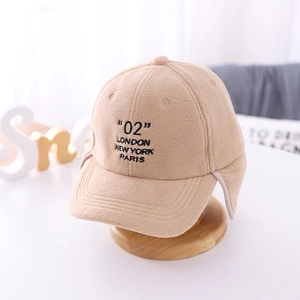 Close-up of beige fleece ear flap cap with city names embroidery on a wooden base