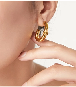 Close-up of gold-plated twisted U-shape earring on ear showing polished texture