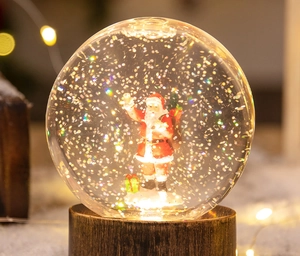 Gros plan d'une boule à neige Père Noël avec socle en bois et paillettes lumineuses