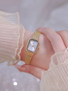 Detail of elegant gold woven mesh strap watch with crystal rectangular dial on model wrist