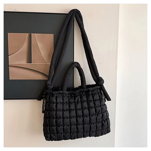 Detail of black quilted puffer tote bag with knotted shoulder strap on white wall
