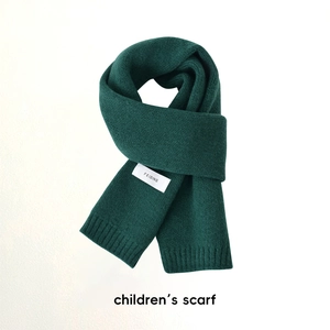 Détail d'une écharpe en maille vert foncé pour enfant avec étiquette sur fond blanc