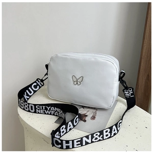 Detail of white nylon crossbody bag featuring silver butterfly buckle and wide lettered strap