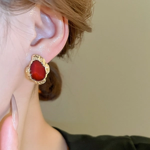 Macro view of vintage oval red resin earrings with gold wavy metal frame on ear